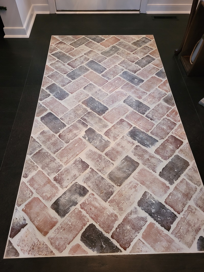 Entryway floor featuring a herringbone brick tile inlay bordered by dark hardwood flooring