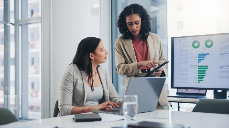 Two professionals review data charts on a screen to apply analytical skills in strategic planning