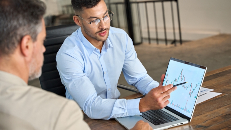 Two professionals review financial charts on a laptop during a business strategy discussion about analytical skills