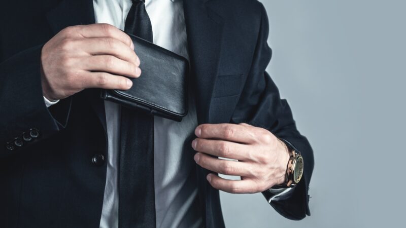 Man in a suit places a black leather wallet inside his jacket pocket