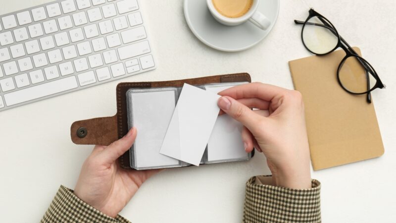 Hands hold cards over an open brown wallet on a desk with coffee and glasses nearby
