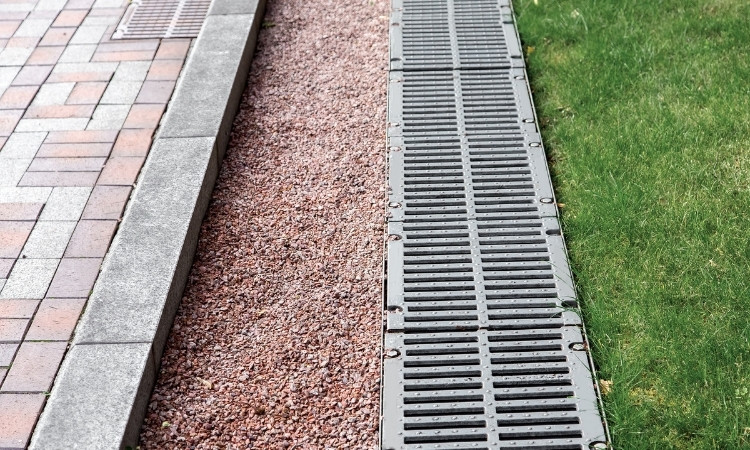 Linear drainage channel between a paved walkway and lawn for directing stormwater runoff.