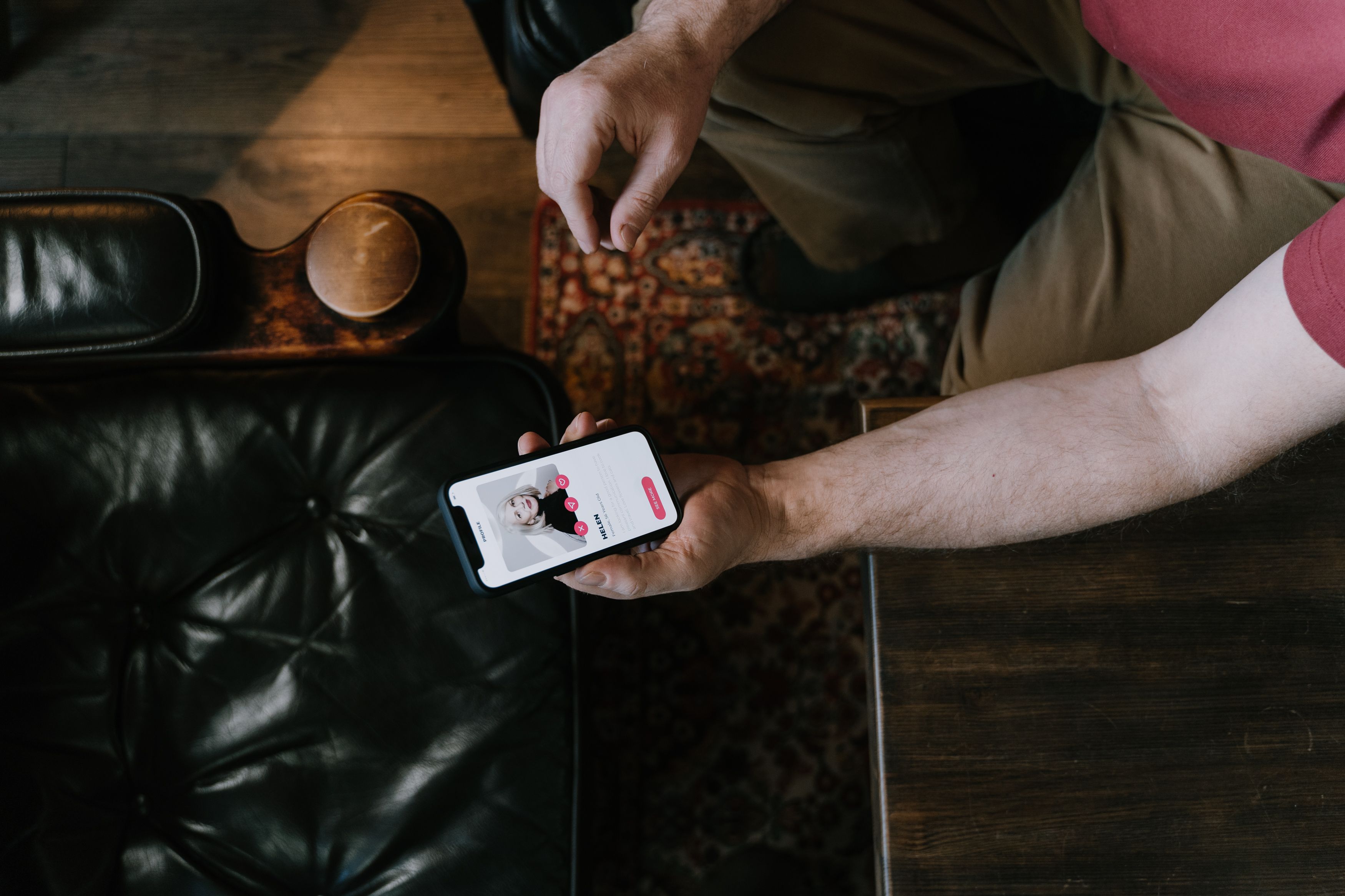 A person holding a smartphone with a dating app displayed while sitting on a leather chair
