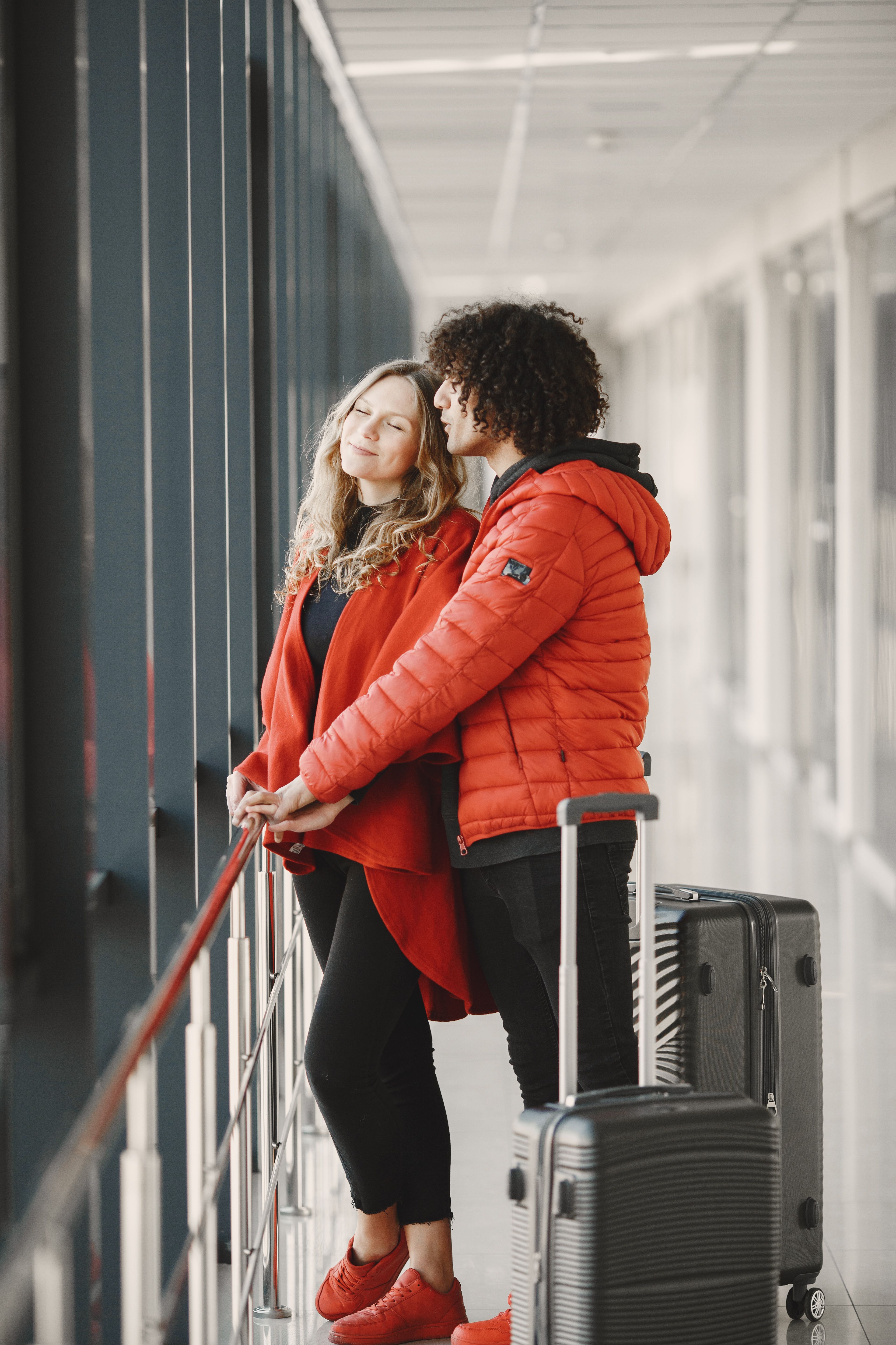 A well-dressed couple standing by a window with luggage, showcasing modern travel style