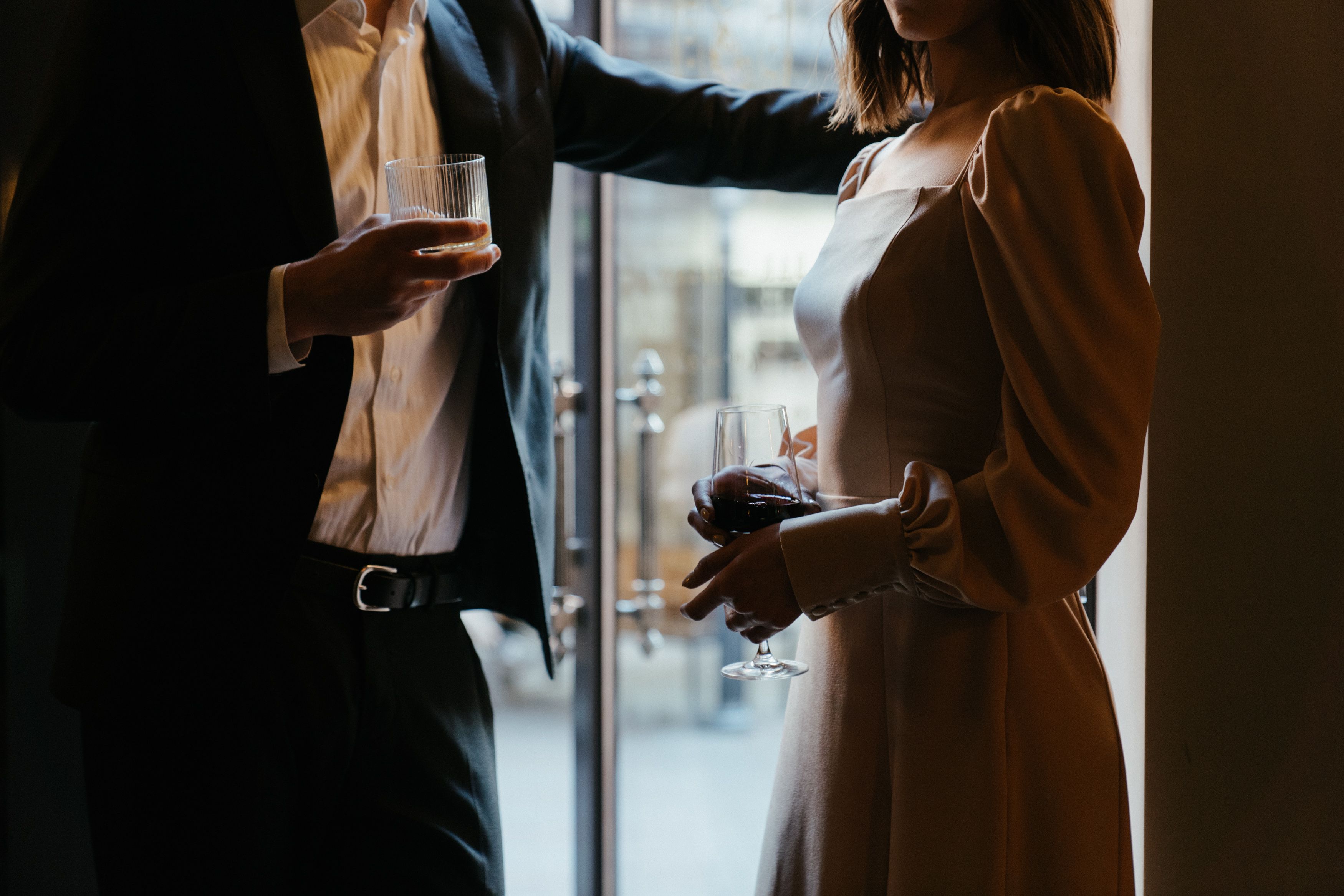 A sophisticated couple in formal attire holding drinks in a moody upscale restaurant atmosphere