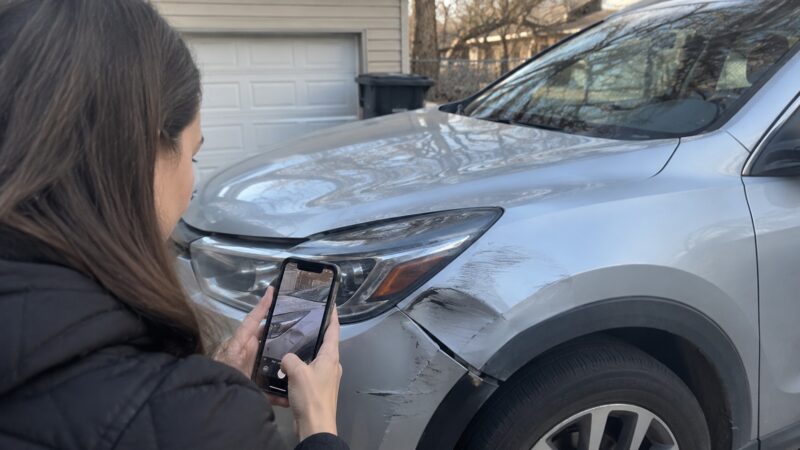 Woman photographing damage to a silver SUV outside her garage.