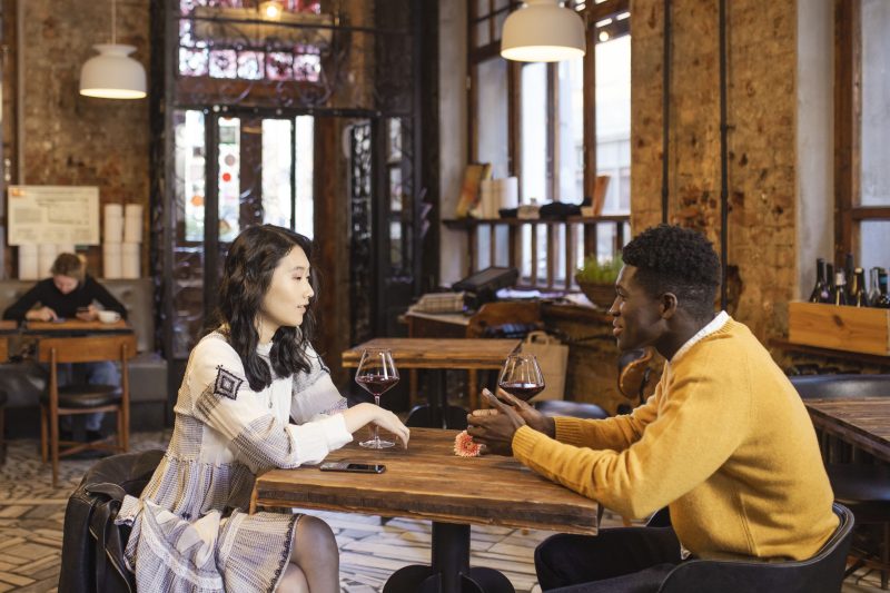 A couple sharing wine and conversation at a stylish cafe, suggesting an intimate companionship experience.