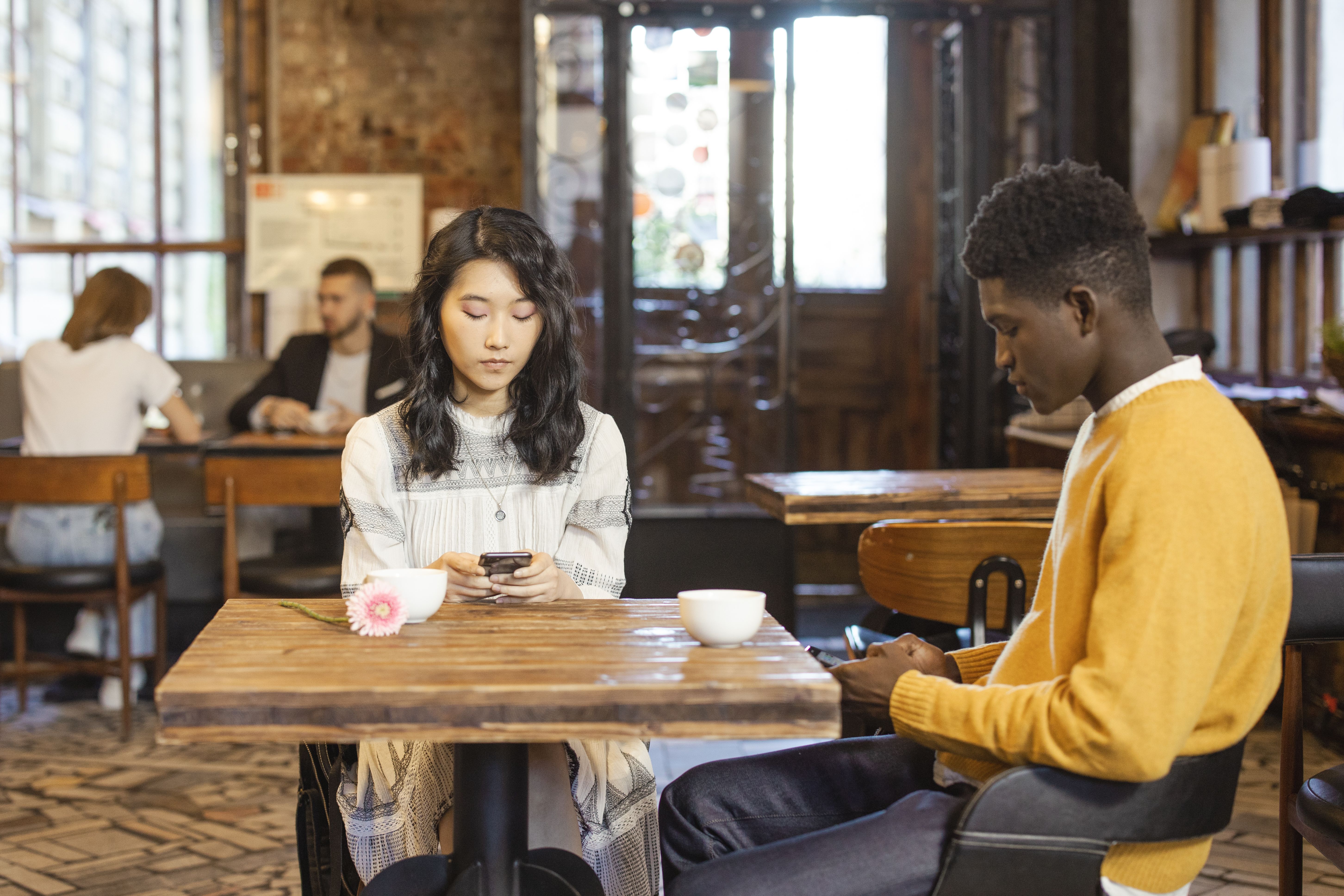 An interracial couple using their phones together at an urban cafe, reflecting modern dating communication.
